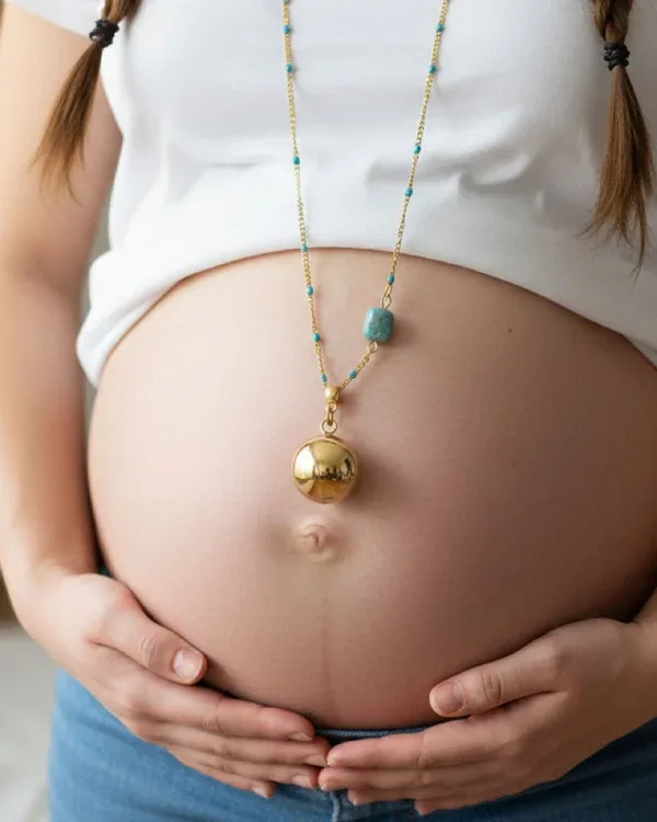 Gold harmony ball necklace on a fine beaded chain resting on a pregnant bump