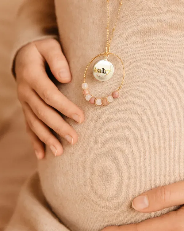Silver harmony ball with an engraved baby medal and a ring of pink gemstone beads on a bump